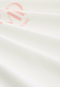 Tissu blanc avec une texture lisse, présentant un logo et un texte rose bien visibles. Le matériau semble léger et légèrement réfléchissant.