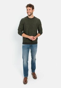 Dark green knit sweater with ribbed cuffs and hem, worn over blue jeans. Brown shoes complement the outfit's casual appearance.