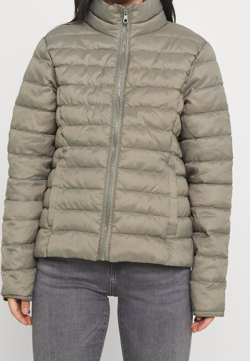Vadderad, zip-up jacka i ljus olivgrön. Har en hög krage och kviltad design med horisontella sömmar. Slät och glänsande textur.