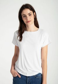 Witte T-shirt met korte mouwen en een ronde halslijn, gemaakt van zacht materiaal, met een losse pasvorm en zichtbare stiksels, gepresenteerd met blauwe denim jeans.