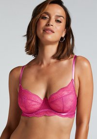 Spitzenrosa BH mit gepolsterten Cups, verstellbaren Satinträgern und gezackten Kanten. Verziert mit Blumenmustern und einer zentralen dekorativen Naht.