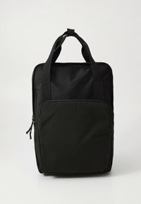 Sort stofrygsæk med to øverste håndtag, en lynlåslomme foran og et minimalistisk design. Tekstureret overflade med robust materiale.