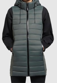 Gilet imbottito verde scuro con zip frontale, cappuccio regolabile e tasche laterali. Presenta cuciture orizzontali e una finitura elegante.