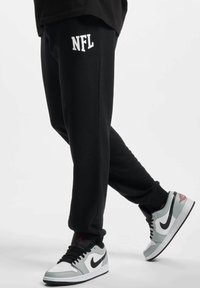 Sorte sweatpants med hvit "NFL" logo, laget av myk stoff. Bært med grå og svarte Nike sneakers, med et klassisk design og detaljer.