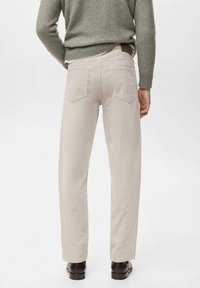 Pantaloni di velluto a coste beige con gamba dritta, due tasche posteriori e tessuto testurizzato. Indossati con un maglione grigio e scarpe scure.