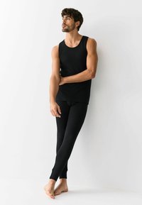 Top nero senza maniche e leggings lunghi abbinati in tessuto a coste. Design aderente, costruzione senza cuciture e texture morbida. Posizione a piedi nudi.