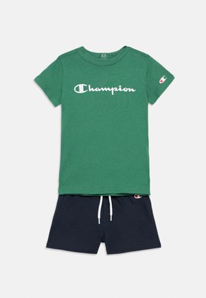 Camiseta Champion verde de manga corta con logo blanco y pantalones cortos azul marino con cordón, que presentan un pequeño logo de Champion en la pierna izquierda.