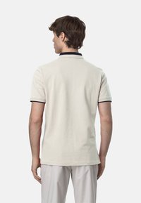 Polo beige con colletto e bordi delle maniche blu navy, maniche corte e orlo dritto. Il materiale sembra morbido e strutturato.
