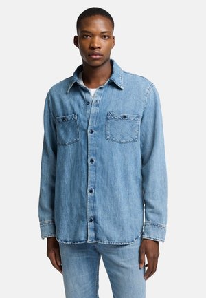 Light blue denim shirt featuring a button-up front, two chest pockets, and a classic collar. Long sleeves with buttoned cuffs.