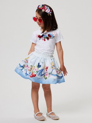 Hvit t-skjorte med blomsterapplikasjoner, blå skjørt med illustrasjoner fra Alice i eventyrland, hjerteformede solbriller og dekorativt hodebånd.