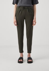 Olivgrüne, taillierte Hose mit Kordelzug, Falten und seitlichen Taschen. Getragen mit schwarzen flachen Sandalen. Glatte Stoffoberfläche.