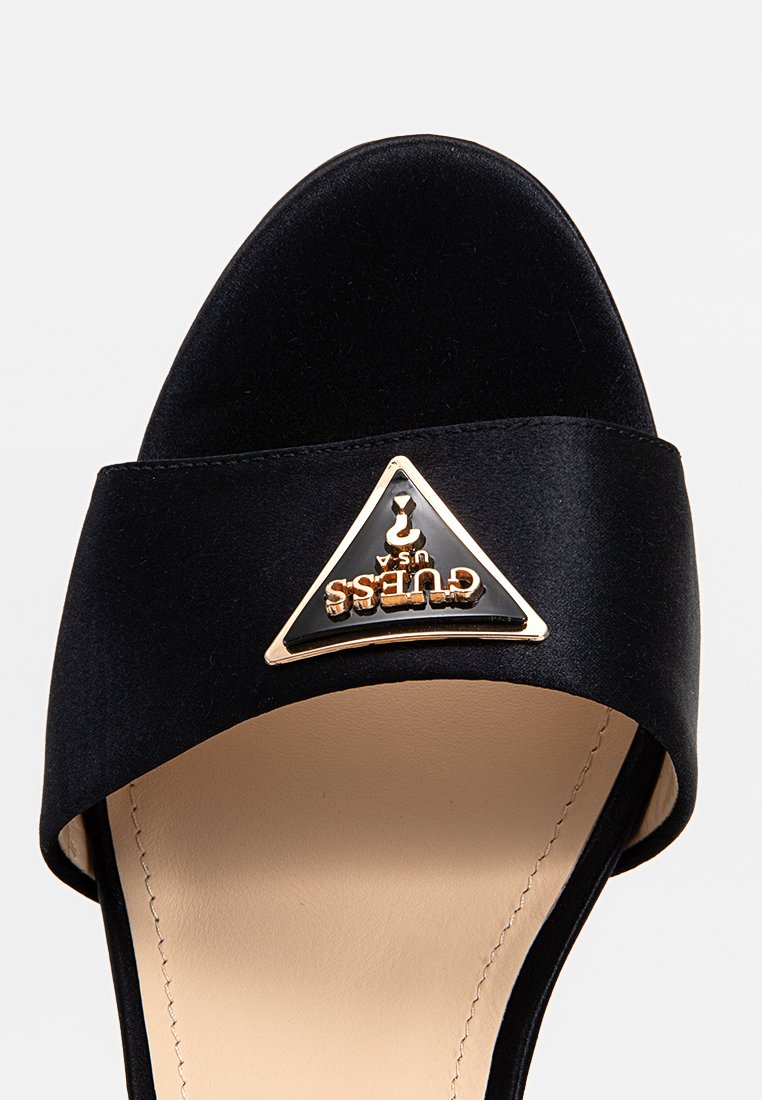 Sandale à talons ouverts noires avec semelle intérieure beige et logo Guess USA en triangle orné d'accent sur la lanière.