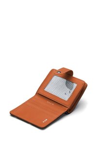 Orange leather wallet with a clear ID window, interior card slots, and textured lining, featuring white zigzag patterns and embossed brand name.