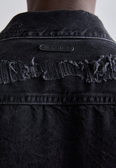 Jachetă din denim negru cu guler distrus, având margini desfăcute și un etichetă de marcă mată de culoare neagră, cu inscripția "HELMUT LANG" pe spate.