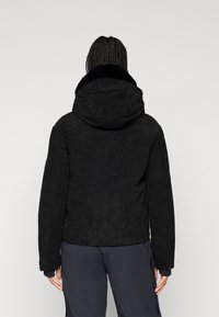 Černá kordurová bunda s kapucí a texturovaným povrchem, nabízející pohodlný límec a dobře padnoucí střih. Doplněná dlouhými rukávy.