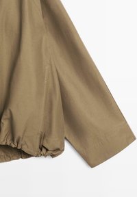 Brauner Stoffjackenärmel mit elastischem Bündchen und sichtbarer Seitennähte auf weißem Hintergrund.