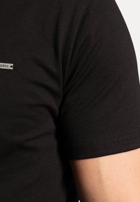 Czarny t-shirt z krótkim rękawem wykonany z gładkiego materiału, z dyskretną metką logo oraz starannie wykończonymi detalami na rękawie i boku.