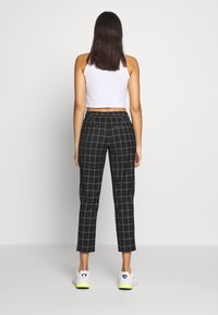 Black checkered trousers with a tailored fit, featuring a mid-rise waist and side pockets, paired with white sneakers and a cropped top.