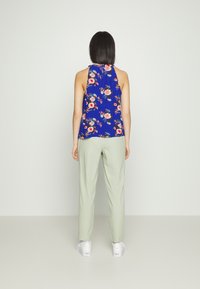 Top sem mangas com padrão floral em azul, combinado com calças verde-claro. O conjunto apresenta um design descontraído e calçado atlético.