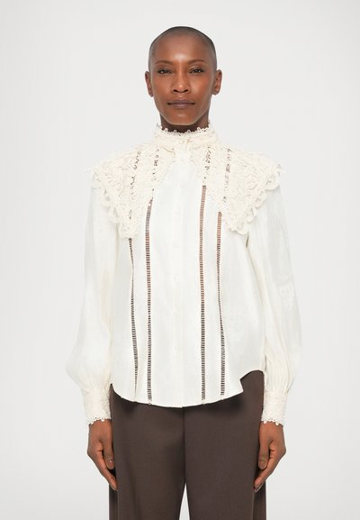 White blouse with textured lace collar and cuffs, vertical stripes, and button closures. Fabric appears light and slightly sheer.