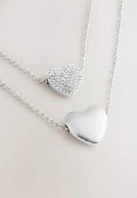 Collier en pendentif en argent en forme de cœur, comprenant un cœur à la finition lisse et un autre orné de strass clairs, suspendu �à une chaîne.