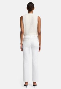 Kremowa bezrękawnikowa bluzka dziergana w połączeniu z białymi jeansami o wysokim stanie. Jeansy mają kieszenie z przodu i prosty krój nogawki, podkreślone jasnym przeszyciem.