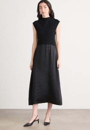 Abito nero con corpino aderente e gonna in satin a forma di A. Caratterizzato da un design senza maniche e scollatura alta. Abbinato a tacchi slingback neri.
