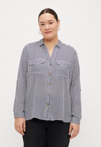 Chemise à manches longues à rayures bleu marine et blanches, dotée de deux poches poitrine et de boutons dorés, fabriquée en tissu léger.