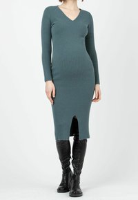 Ribbad teal klänning med V-urringning, långa ärmar och längd till mitten av vaden med en framskjutning, som matchas med knähöga svarta stövlar.