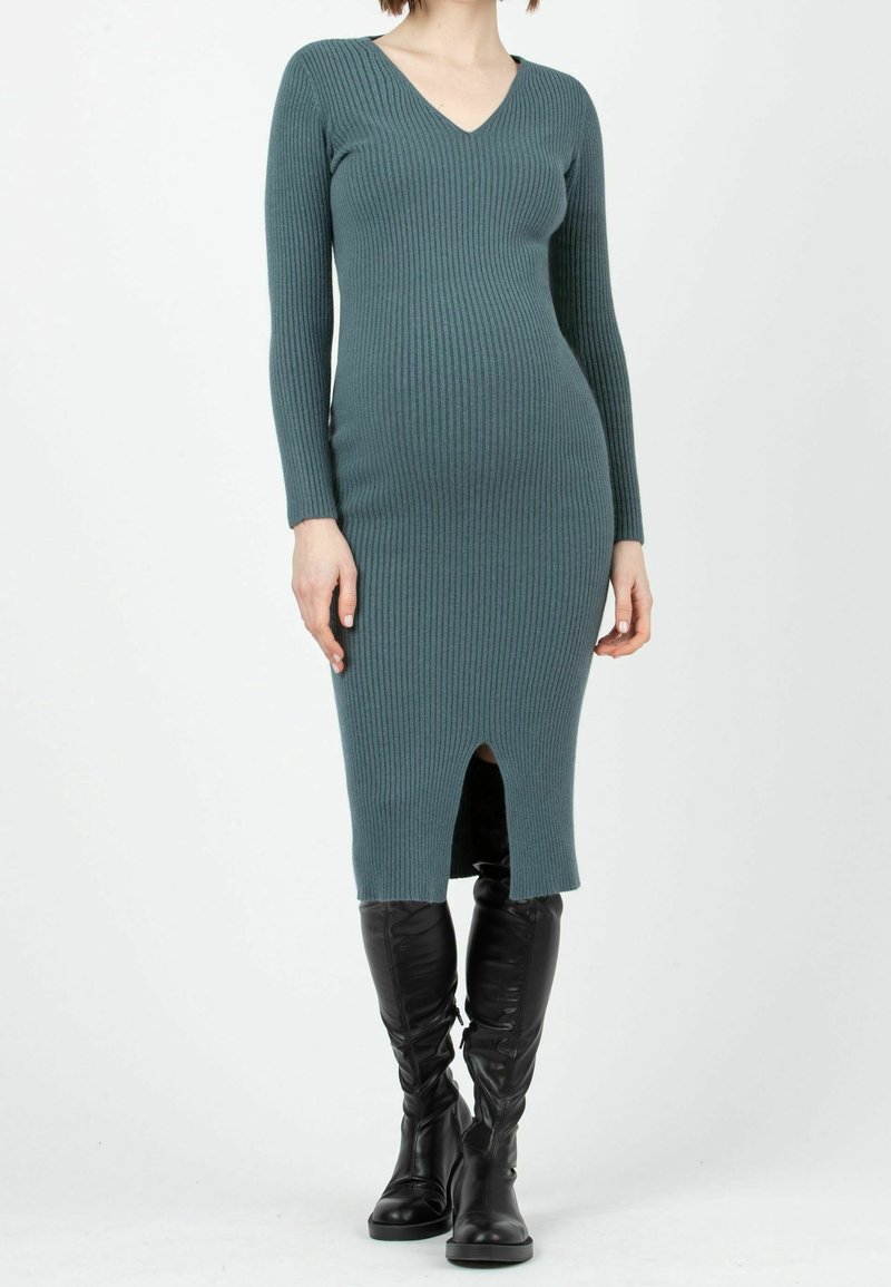 Ribbad teal klänning med V-urringning, långa ärmar och längd till mitten av vaden med en framskjutning, som matchas med knähöga svarta stövlar.