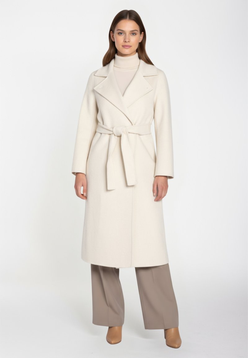 Cappotto lungo color crema con vita cintrata e rever a scollo a V. Presenta maniche lunghe e una silhouette dritta, abbinato a pantaloni color taupe.