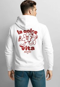 Mann trägt einen weißen Hoodie mit einer roten Cartoon-Blume, hält ein Glas und eine Flasche, mit dem Text "la dolce vita" und "Neverless" auf dem Rücken.