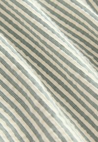Változó, keskeny, sötétzöld és krémszínű csíkos mintázatú textil; az anyag puhanak tűnik, enyhén struktúrával. 