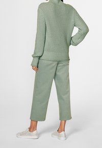 Pull à col roulé en maille vert clair avec une coupe ample, associé à un pantalon large en velours côtelé assorti et des baskets blanches.