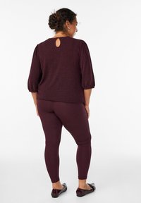 Top bordeaux con texture, maniche a palloncino e dettaglio a chiave sulla schiena, abbinato a leggings aderenti coordinati e ballerine scure.
