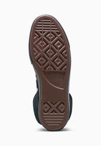 Zapatilla de lona negra con suela de goma marrón, que presenta una suela con un dibujo de rombos y ojales plateados para los cordones. Marca Converse All Star visible.