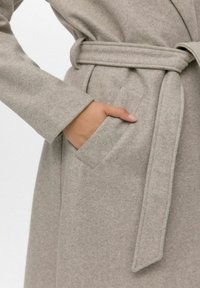 Cappotto grigio chiaro in misto lana con vita regolabile, maniche lunghe e tasca laterale. Texture morbida con una finitura liscia.