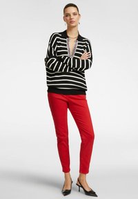 Suéter de rayas blanco y negro con escote en V y detalles rojos, combinado con pantalones rojos ajustados y tacones negros puntiagudos. Texturas suaves.