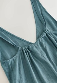 Haut bleu sans manches avec encolure froncée et fines rayures verticales texturées sur un tissu léger.