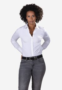Weißes Hemd mit Kragen, kombiniert mit grauen Jeans und einem schwarzen Gürtel. Das Hemd hat lange Ärmel und eine figurnahe Passform.