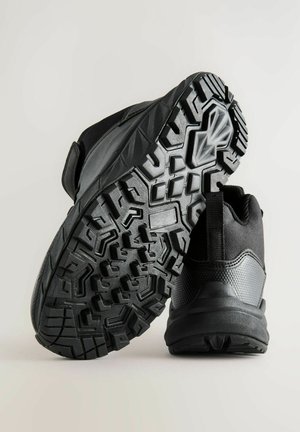 Zwarte sportieve schoenen met een gestructureerde bovenkant en een robuuste rubberen buitenzool met een gedetailleerd profiel voor verbeterde grip.