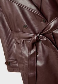 Trench-coat en cuir marron foncé avec des boutons croisés et une ceinture nouée à la taille, montrant des coutures détaillées et une texture lisse.