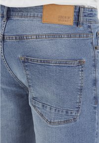 Jeans de mezclilla en azul claro con un acabado texturizado, que cuentan con una etiqueta de cuero que dice "El Viaje del Denim" y bolsillos traseros dobles.