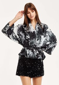 Black and white patterned blouse with a loose fit, button-down front, and tie waist, paired with a short sequin black skirt.