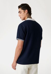 Polo navy con ribetes blancos en el cuello y las mangas. Tejido suave, corte holgado, mangas cortas y textura acanalada.