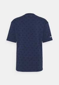 Camiseta azul marino con un patrón repetido de flores de lis y el texto "P. R. I. S" en un diseño sutil, en relieve. Mangas cortas, cuello redondo.