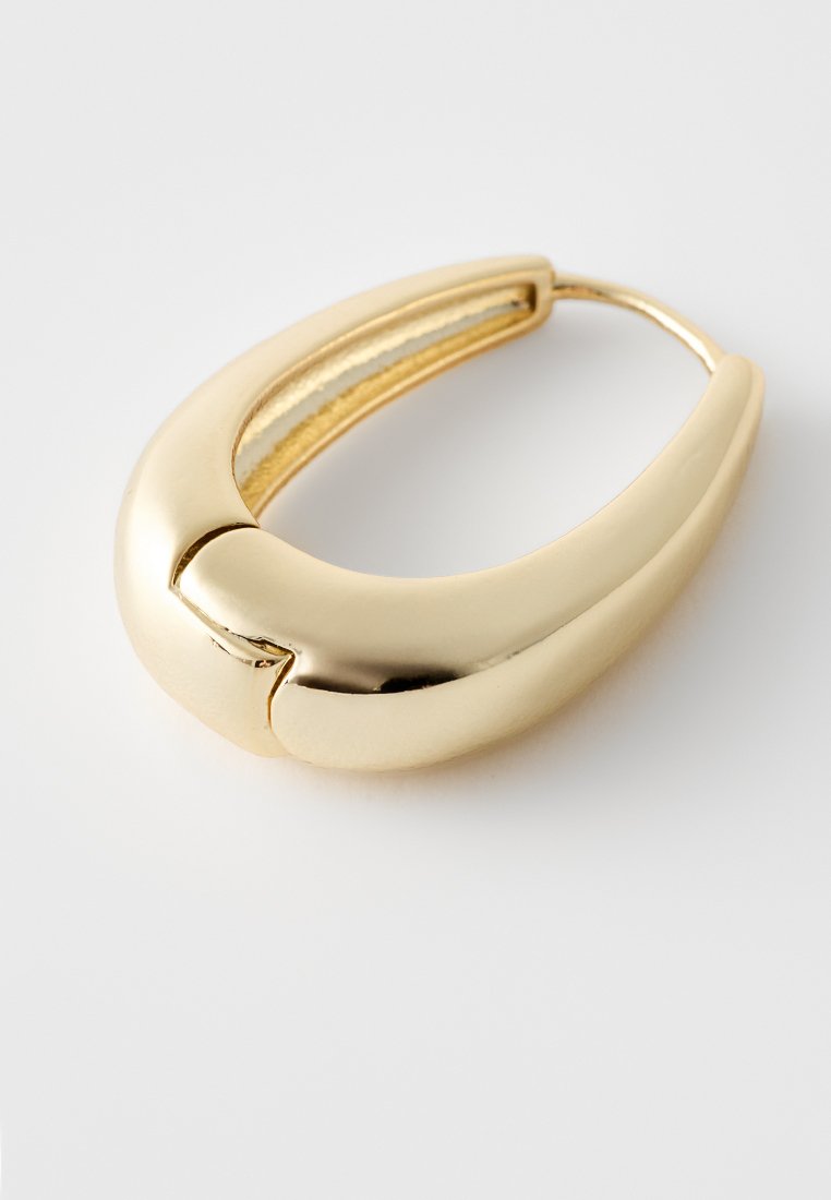 Goldener Creolenohrring mit einem glatten, geschwungenen Design. Verfügt über eine glänzende Metalloberfläche und eine subtil verbundene Öffnung auf einer Seite.