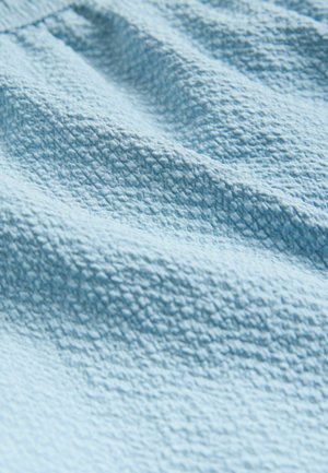 Textúrovaná svetlomodrá textília s jemným tkaným vzorom, ktorá zobrazuje mäkký, zvrásnený povrch s jemnými záhybmi.