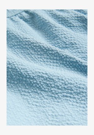 Getextureerde lichtblauwe stof met een subtiel geweven patroon, die een zachte, gekreukte oppervlakte toont die oplicht in zachte plooien.