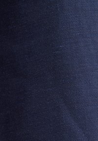 Tissu bleu foncé avec un motif tissé texturé et un léger éclat, montrant de fins fils horizontaux et verticaux.